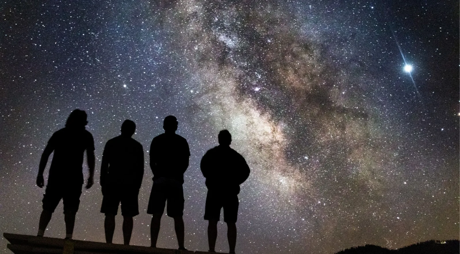 Four guests silhouetted against the full Milky Way arch on a clear night at Mauna Kea