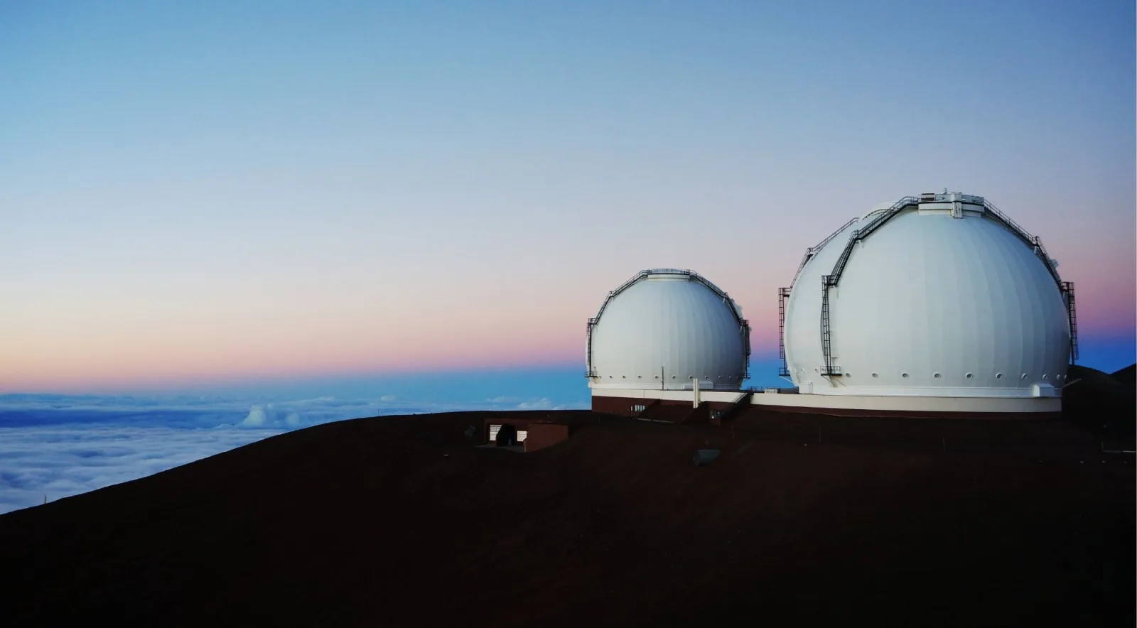 Mauna Kea Observatory domes at twilight with pink and blue sky and a sea of clouds below at 13,800 ft