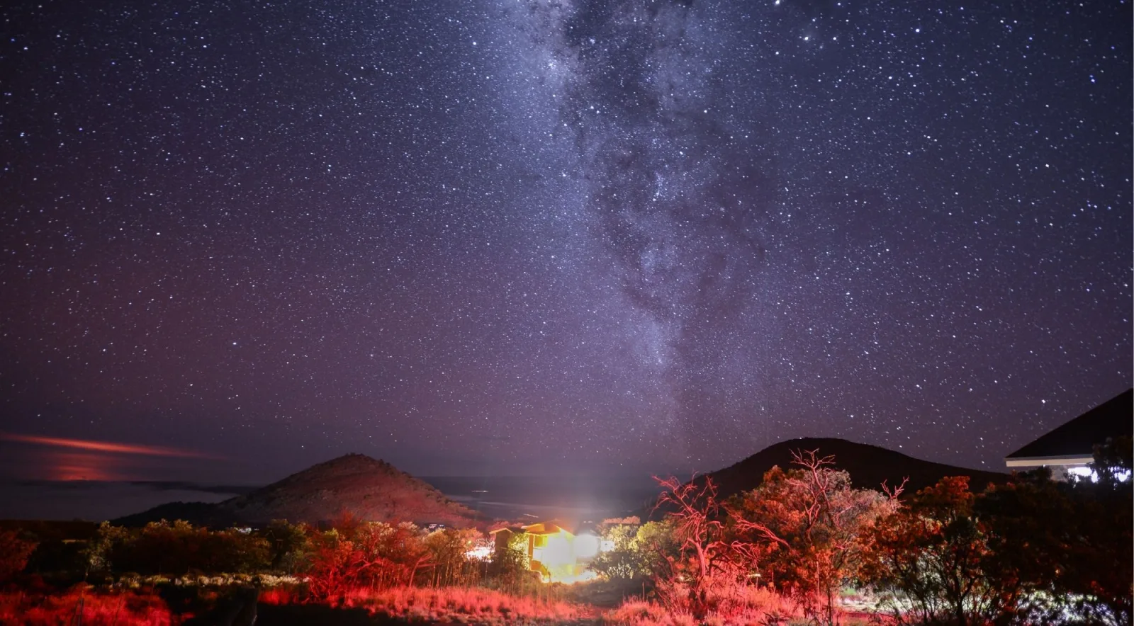 Milky Way rising over Hawaii's Big Island landscape with red-lit vegetation in the foreground