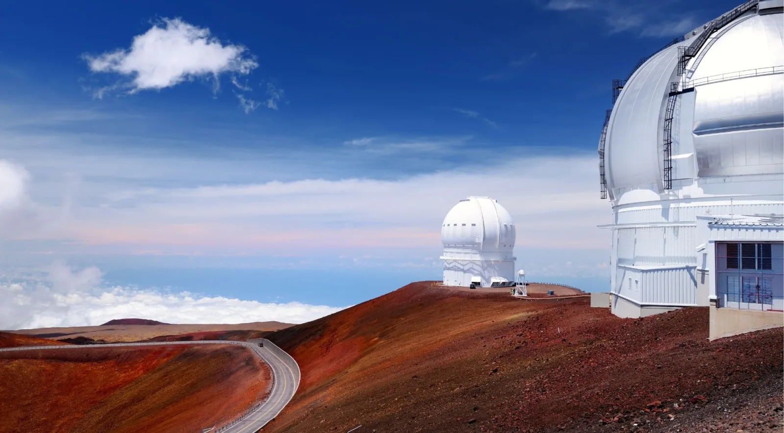 Close-up view of a white Mauna Kea observatory dome above the winding summit access road on red volcanic hillside