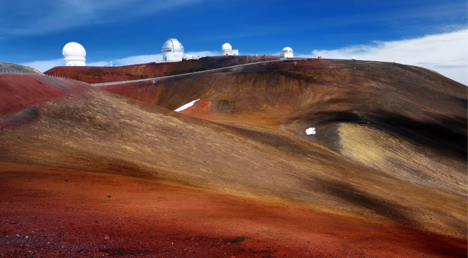 Mauna Kea summit ridge with five observatory domes visible across the red cinder landscape under blue sky