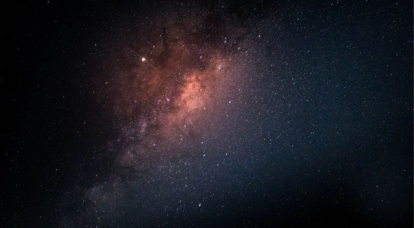 Astrophotography of the Milky Way galactic core showing orange and red nebulae and dark dust lanes from Mauna Kea